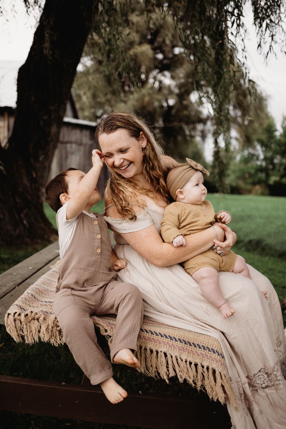 A tender family moment shared on a fringed outdoor bench under a weeping willow tree.