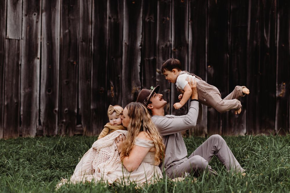A playful family moment captured against a rustic wooden barn backdrop.