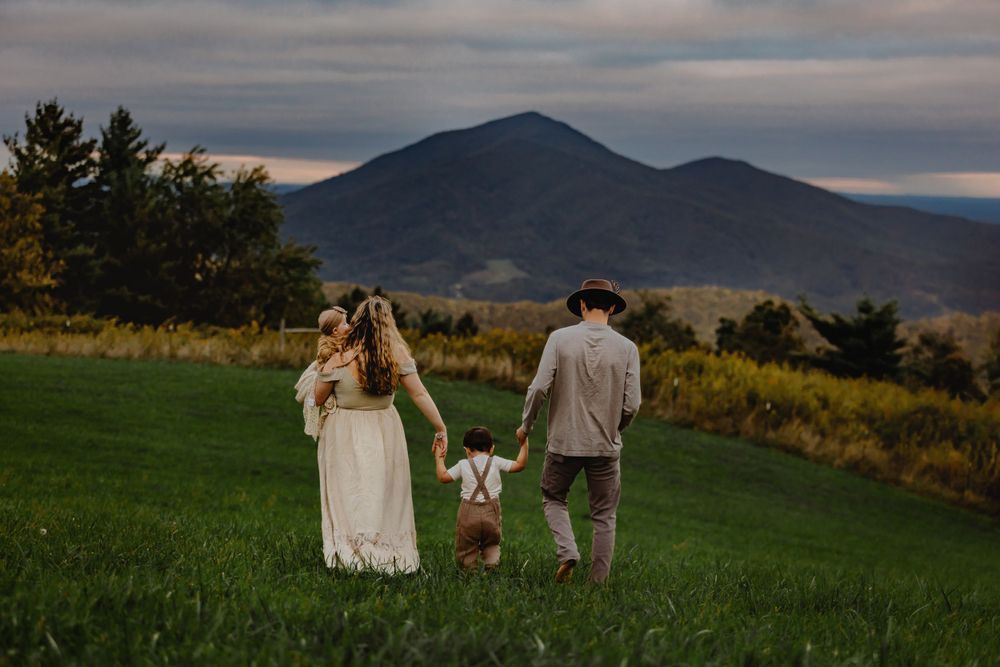 A family walks hand in hand across a hilltop meadow with mountain views at sunset.