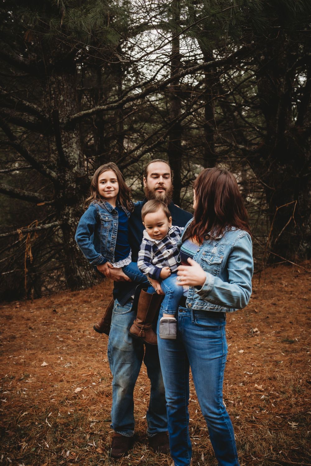 A casual family portrait among tall pine trees in autumn.