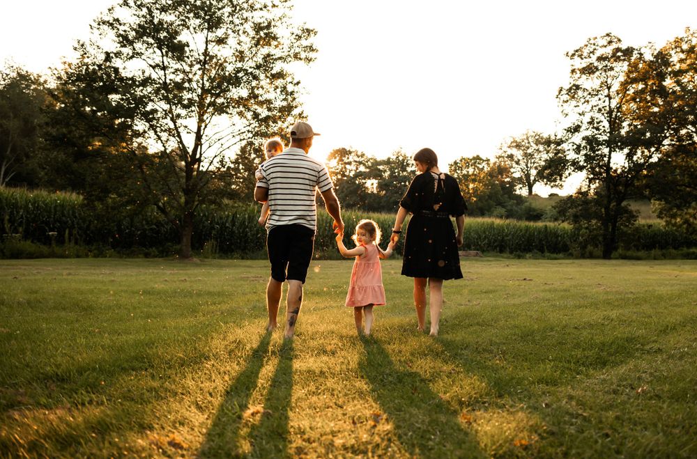 Family walking hand in hand at sunset in a grassy field.
