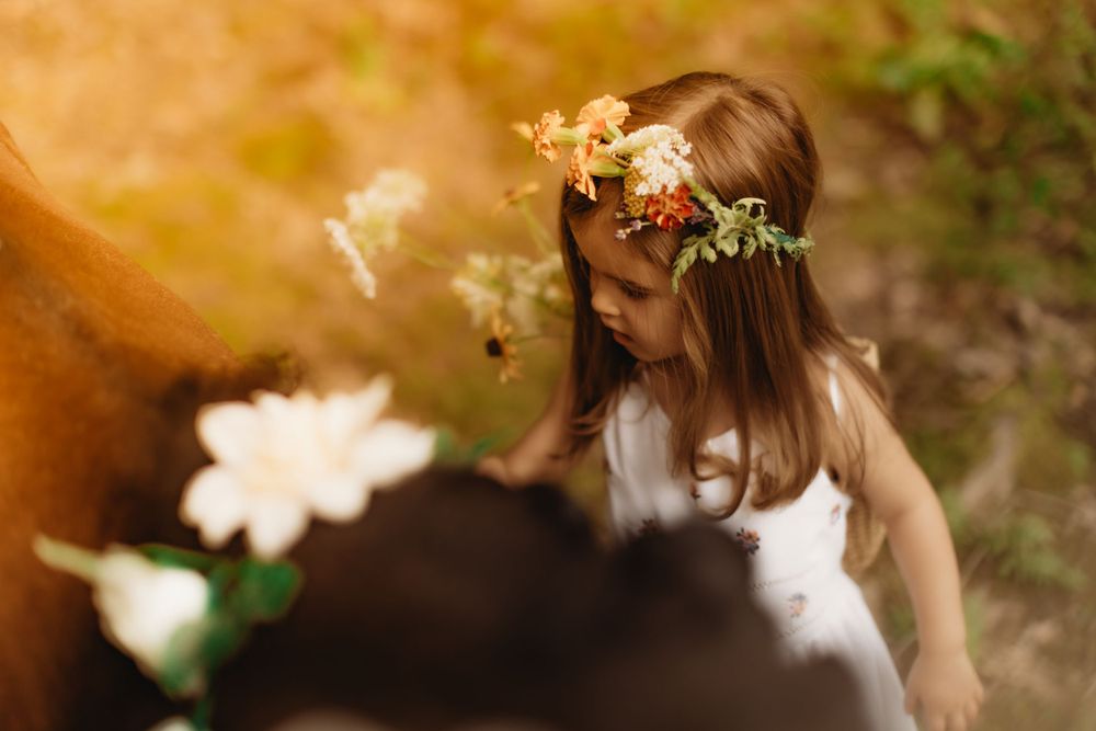 Young person wearing floral crown and white dress in dreamy outdoor setting.
