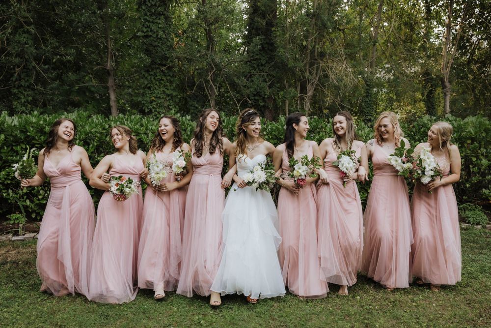 Bridesmaids in blush pink dresses sitting on grass with bride in white.