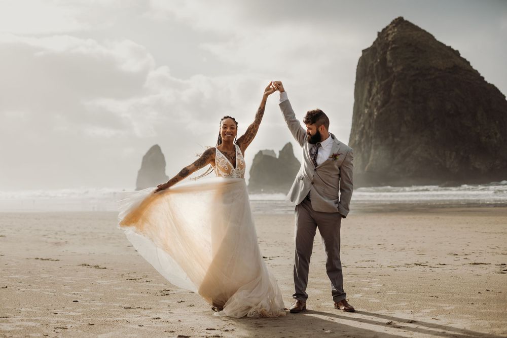 Newlyweds celebrate on a misty beach with flowing white dress and dramatic coastal backdrop.