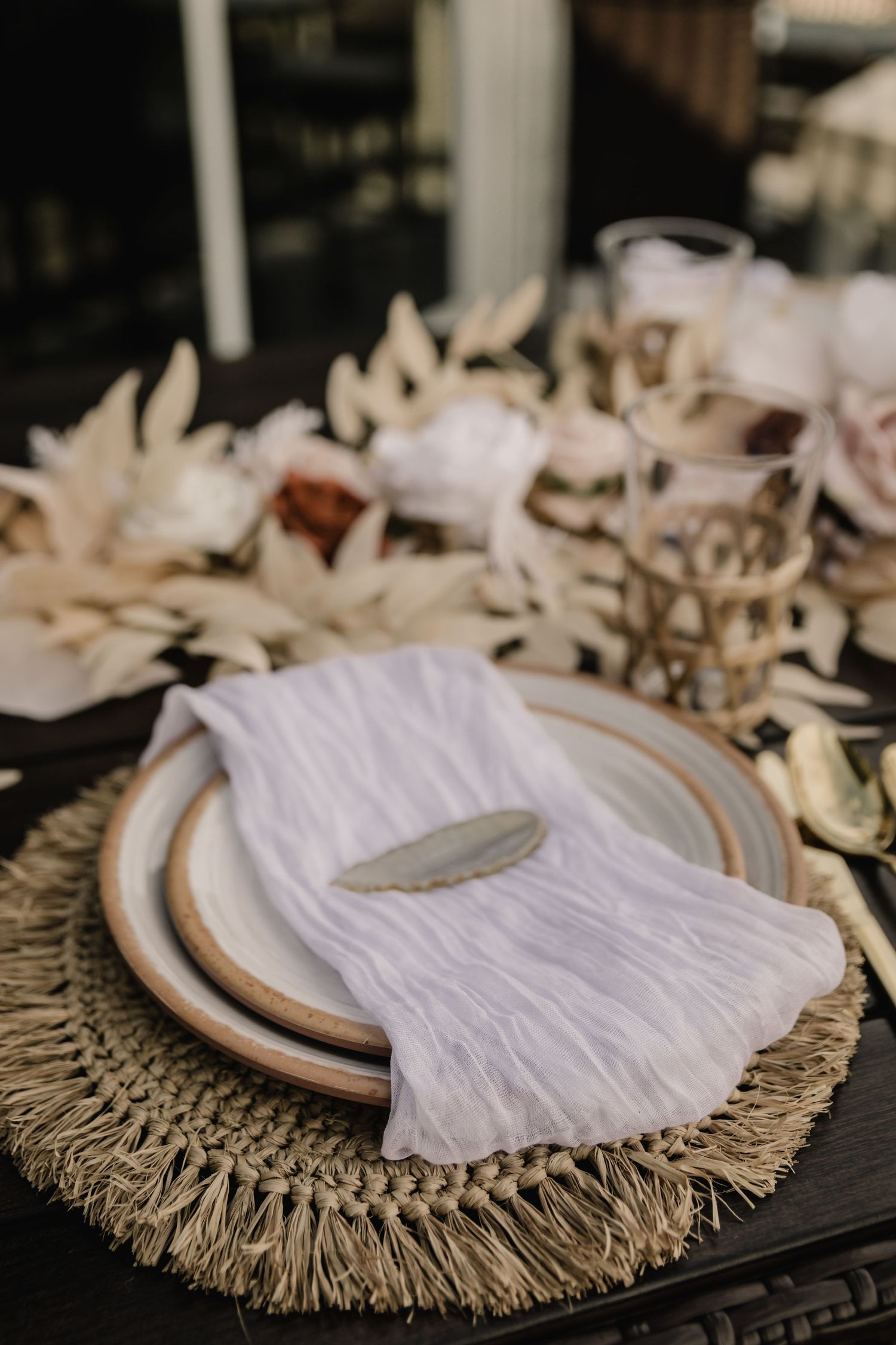 Rustic place setting with white napkin and plate on woven charger mat.