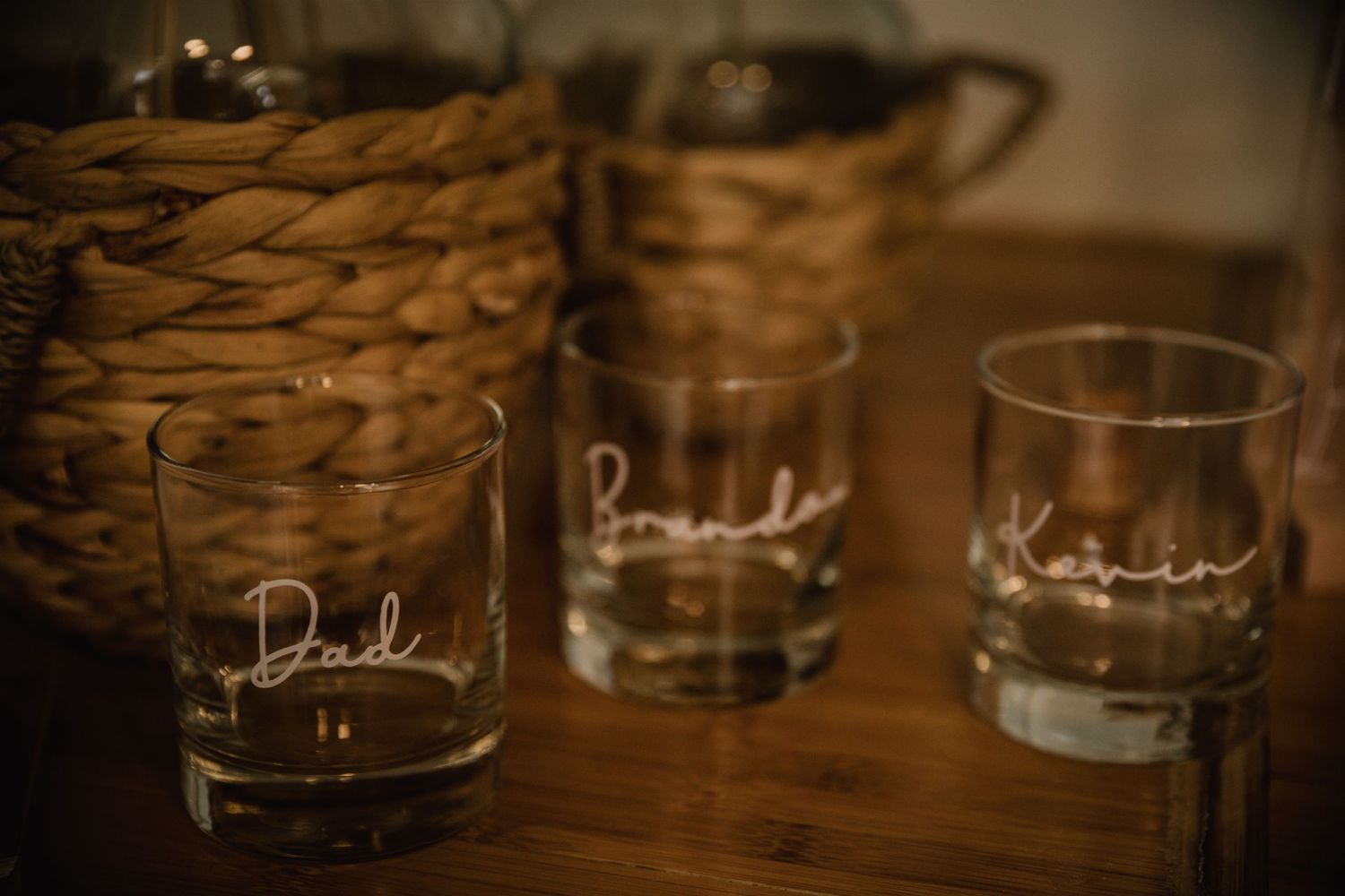 Personalized whiskey glasses with names etched on them displayed on wooden surface.