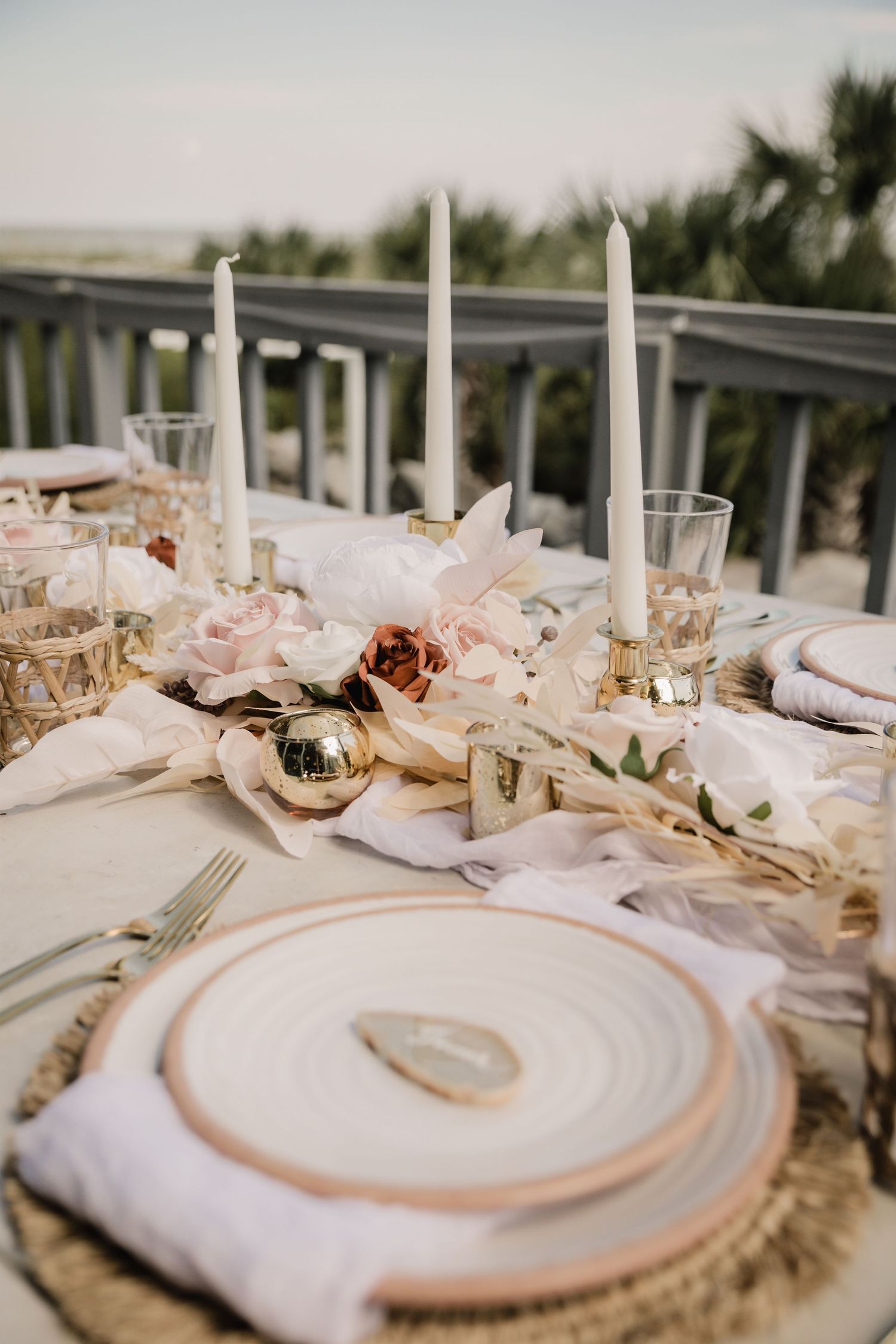Romantic table setting with white candles, pink flowers and gold accents for outdoor wedding reception.