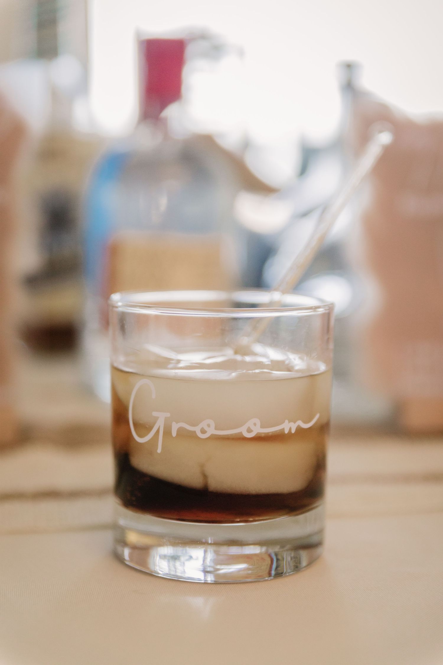 Glass tumbler labeled 'Groom' containing layered cocktail on light colored surface.