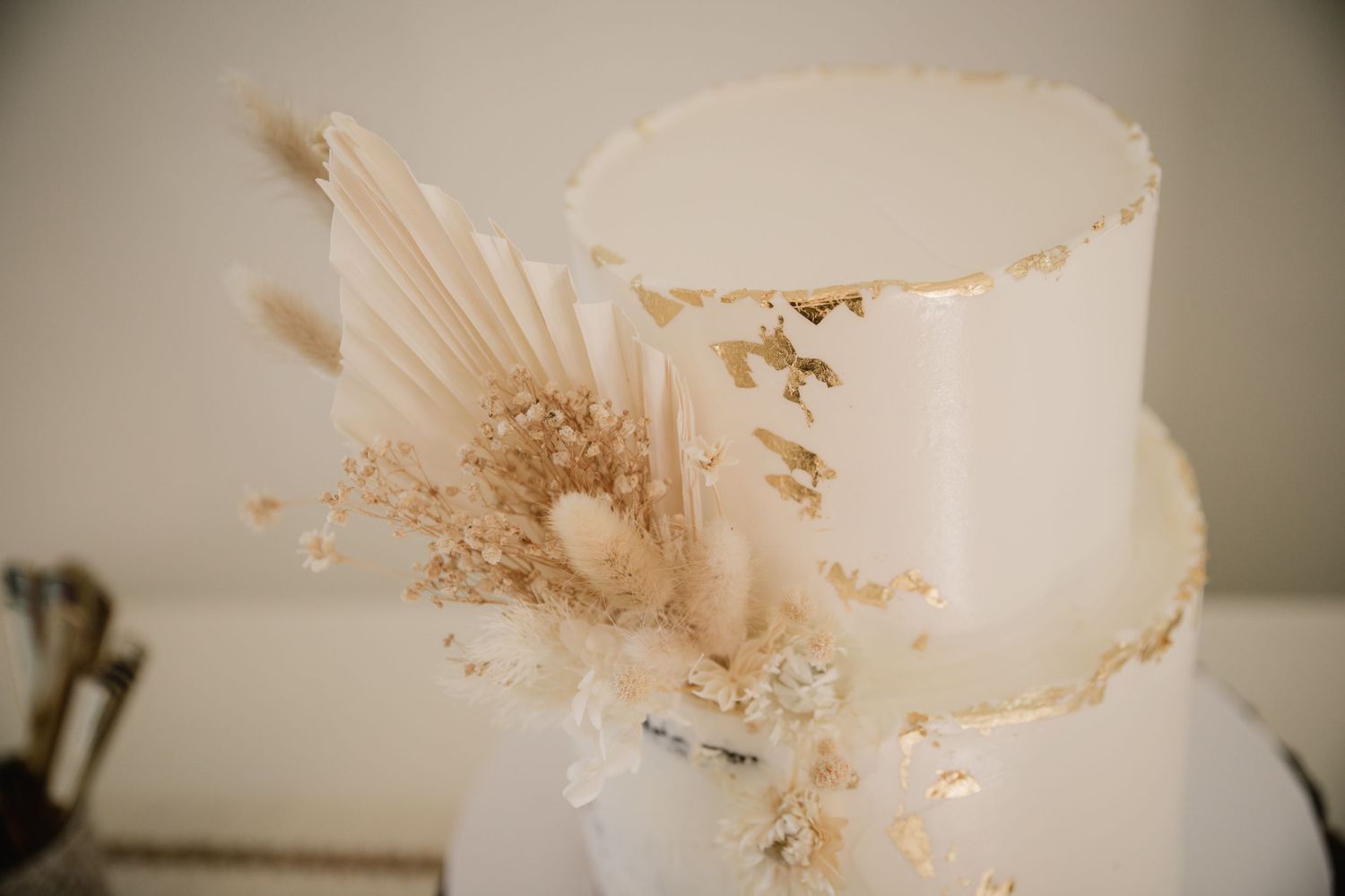 Close-up view of white wedding cake decorated with dried flowers and gold foil details.