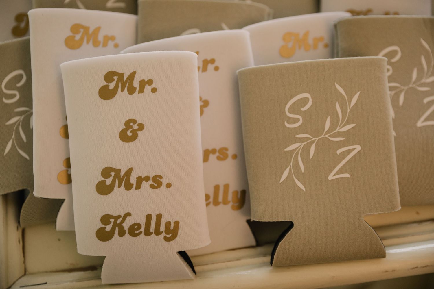 Wedding koozies with Mr. & Mrs. Kelly text in gold lettering arranged on display.