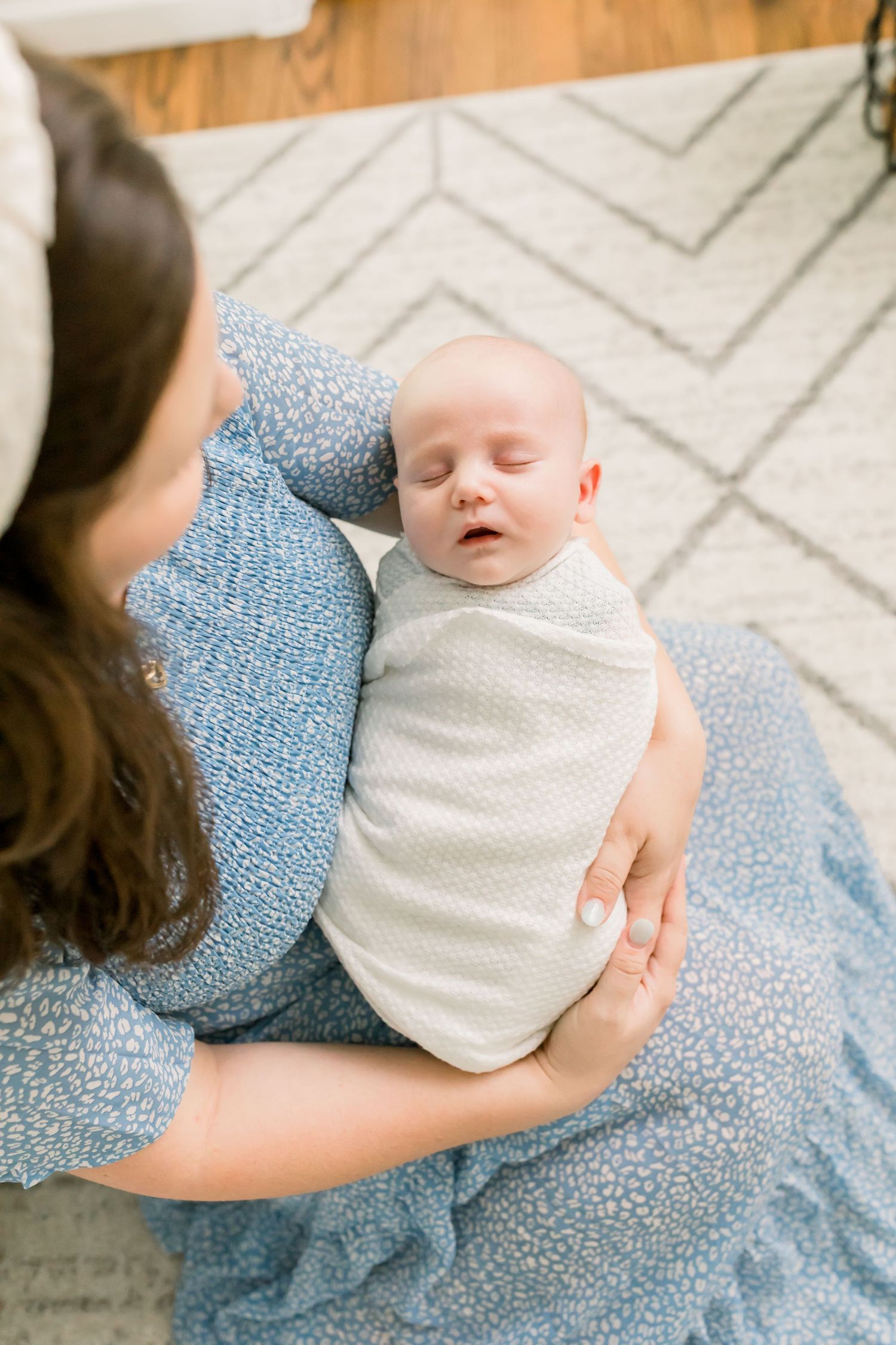 A peaceful sleeping infant swaddled in white resting on a patterned rug.