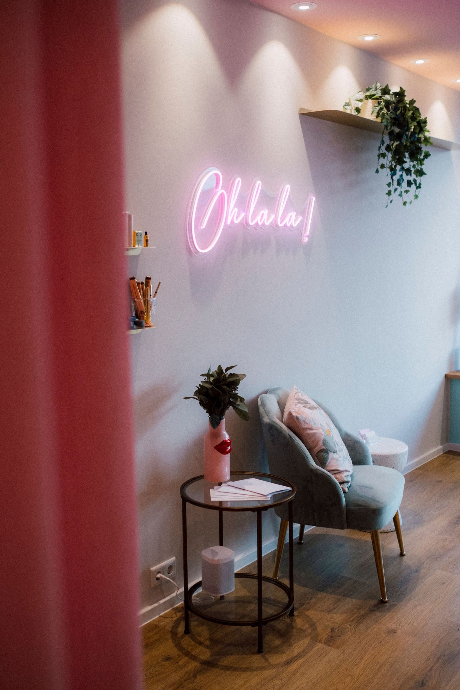 Modern interior space with pink neon sign and cozy grey armchair next to round side table with plants.
