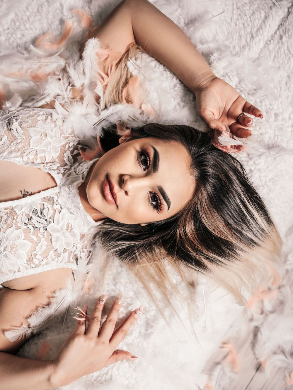 Boudoir photo of a woman on the bed, surrounded by soft feathers, creating an intimate and sensual moment.