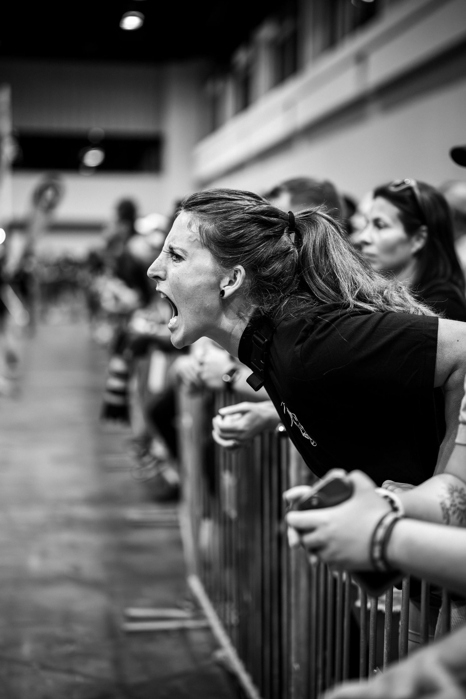 Spectator cheering enthusiastically from behind barrier at indoor sports competition.