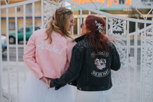 Two friends wearing matching pink and black jackets pose together against a white fence background.