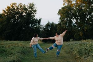 Two people holding hands while playfully running through a grassy field at sunset.