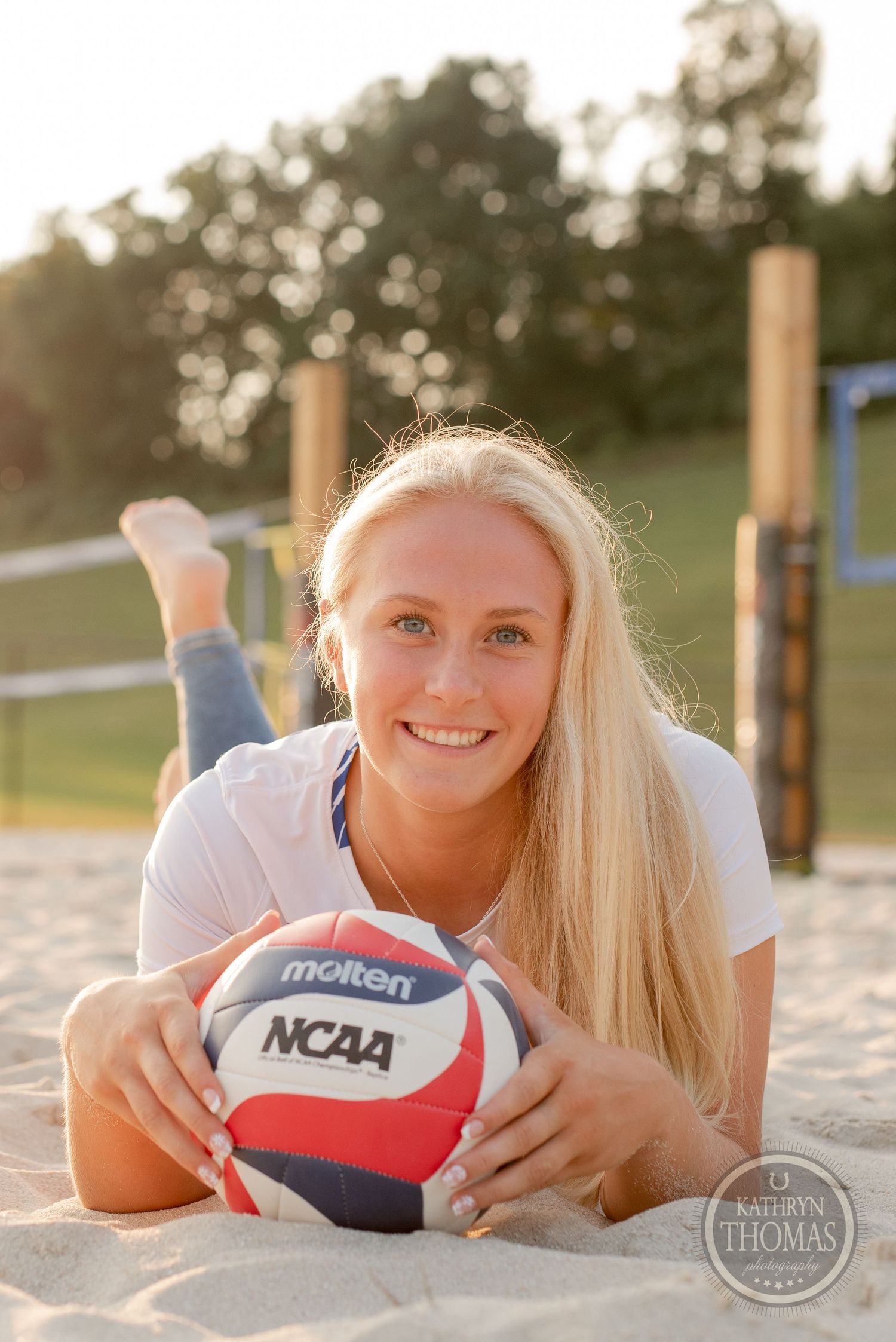 Athlete lying on sand with official NCAA volleyball during sunset photo session.