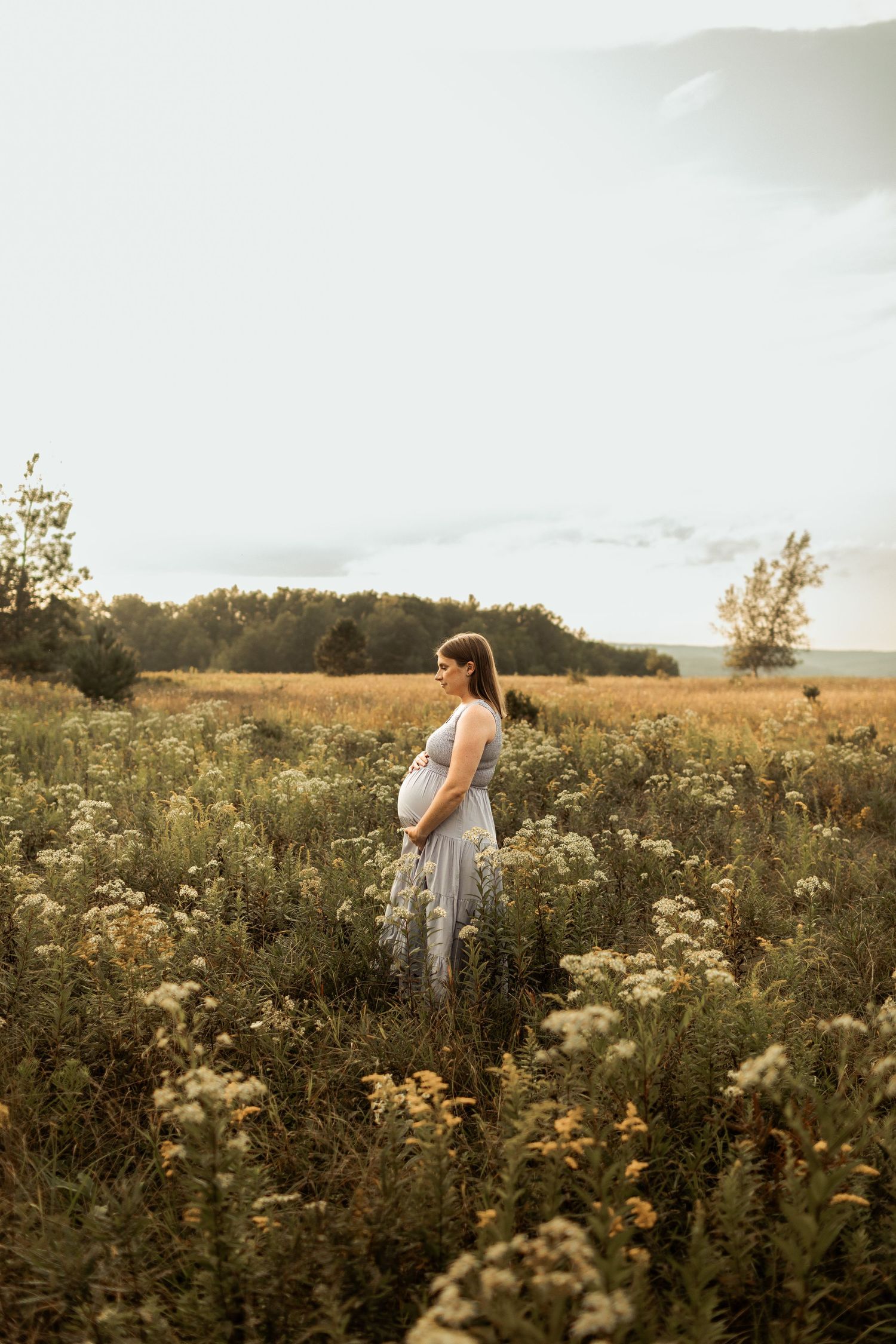 A woman in a flowing dress stands in a wildflower meadow during golden hour.