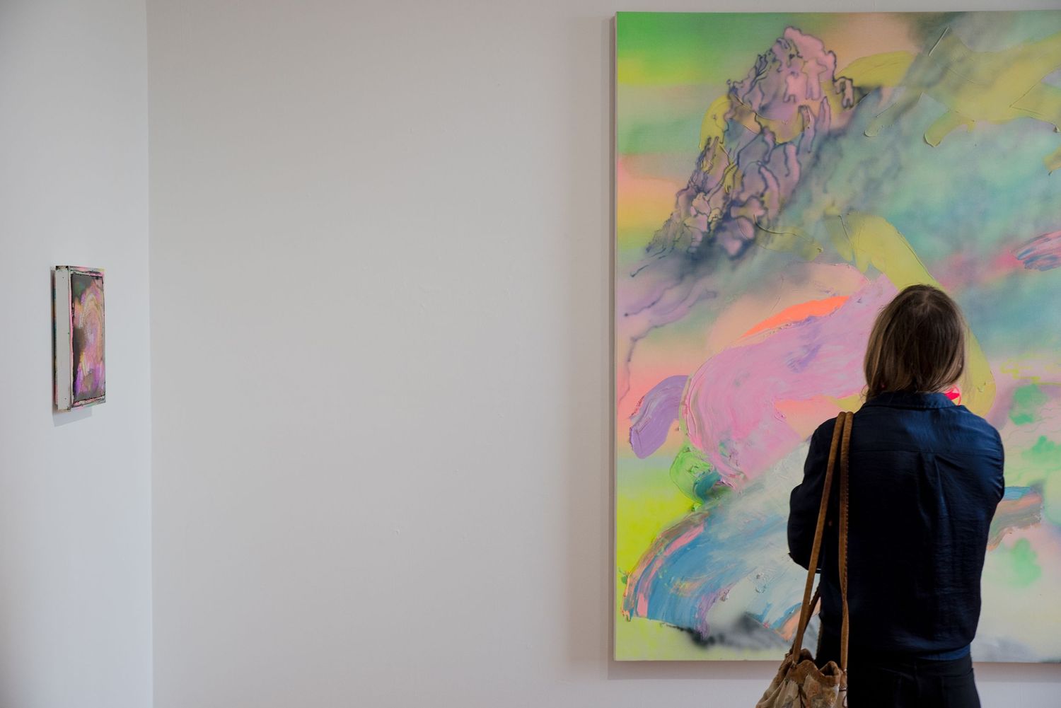Gallery visitor viewing colorful abstract mountain landscape painting on white wall.