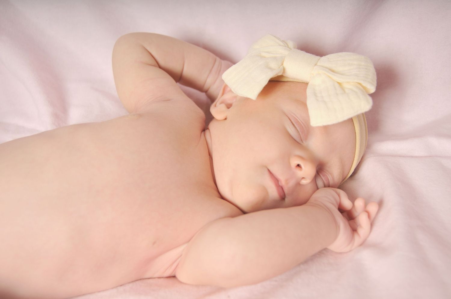 A photo of a naked newborn on pink backdrop