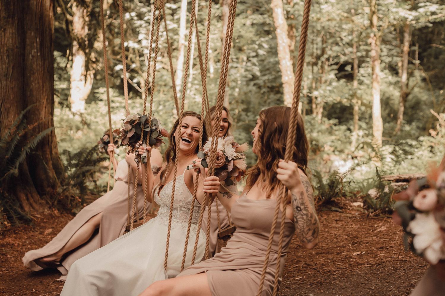 Bridesmaids and bride laughing together on swings, in a lush garden setting.