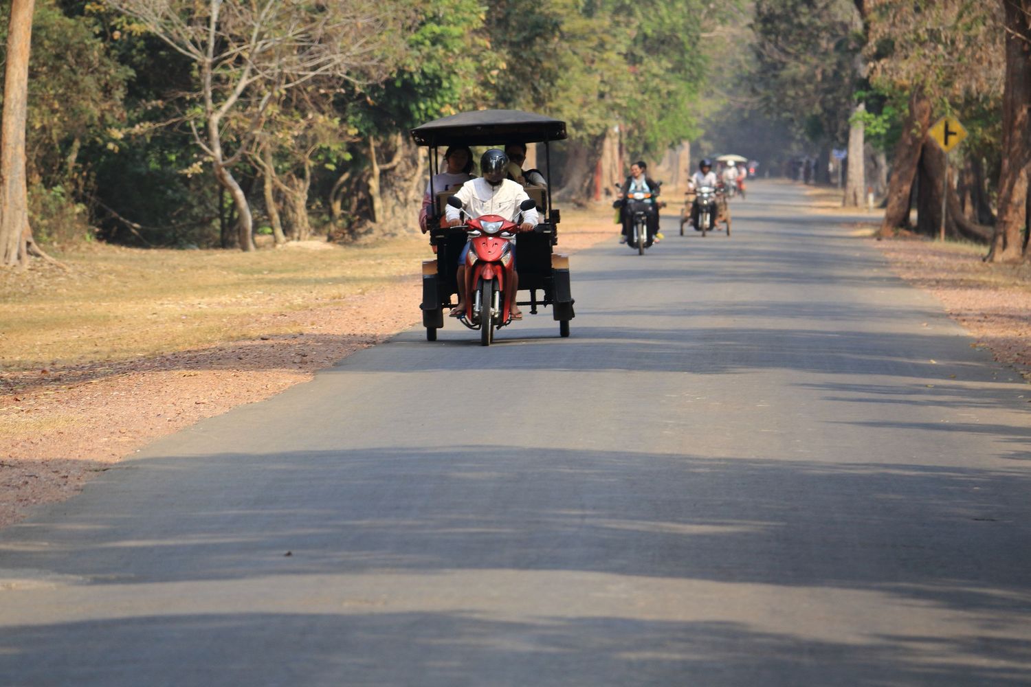 Red tuk tuk driving on a dusty road through temple grounds.