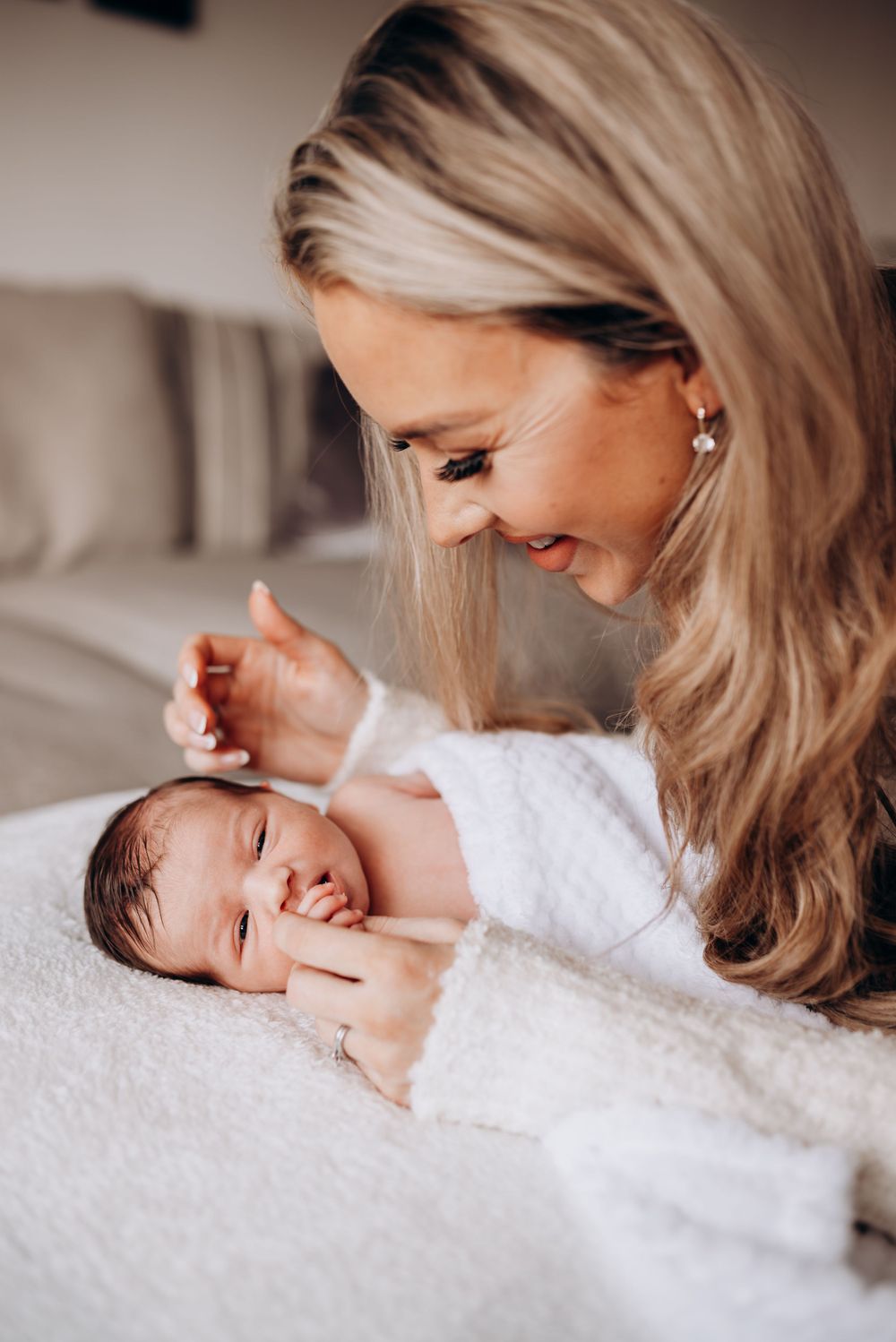 Sweet newborn photography session capturing gentle maternal moments on soft white bedding.