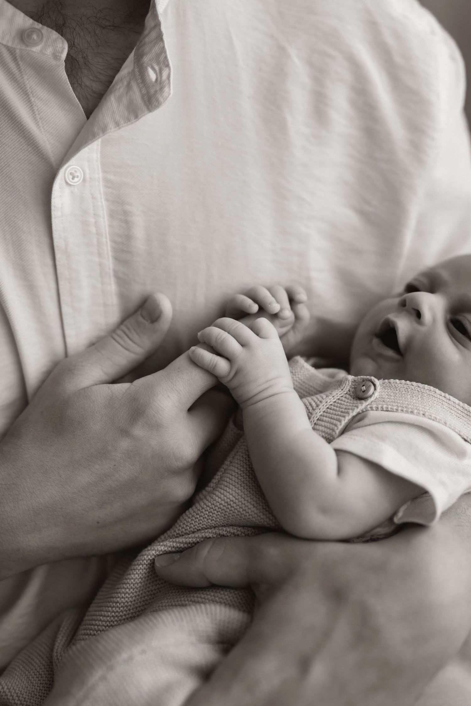 Black and white image capturing playful moment between parent and laughing baby.