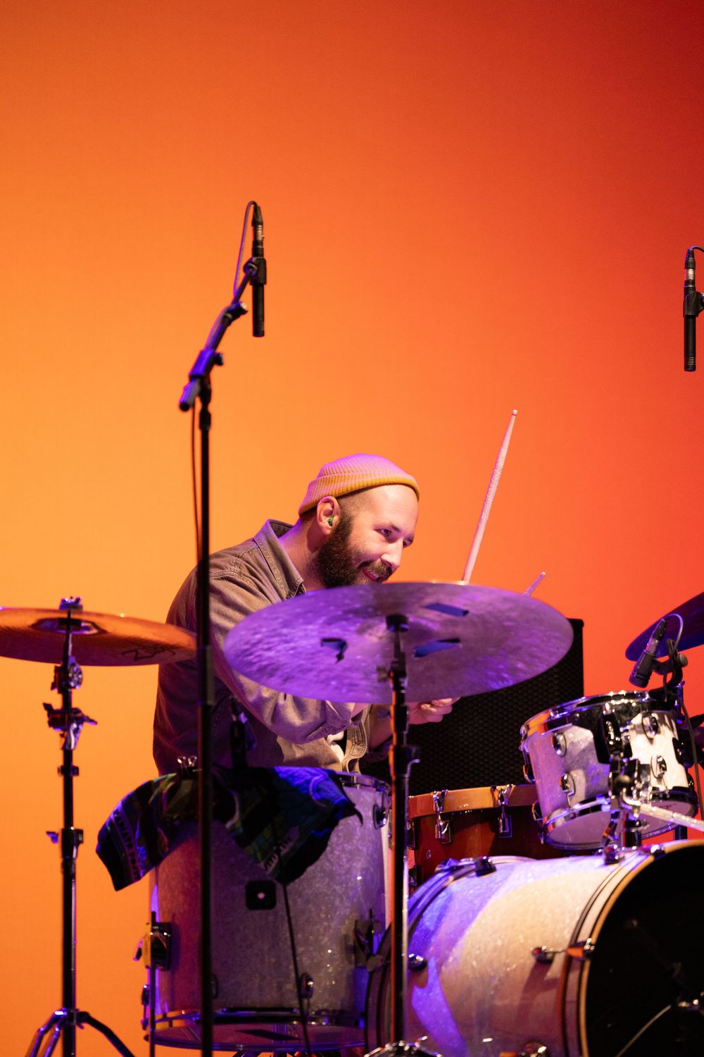 Drummer playing cymbals on drum kit against vibrant orange backdrop.