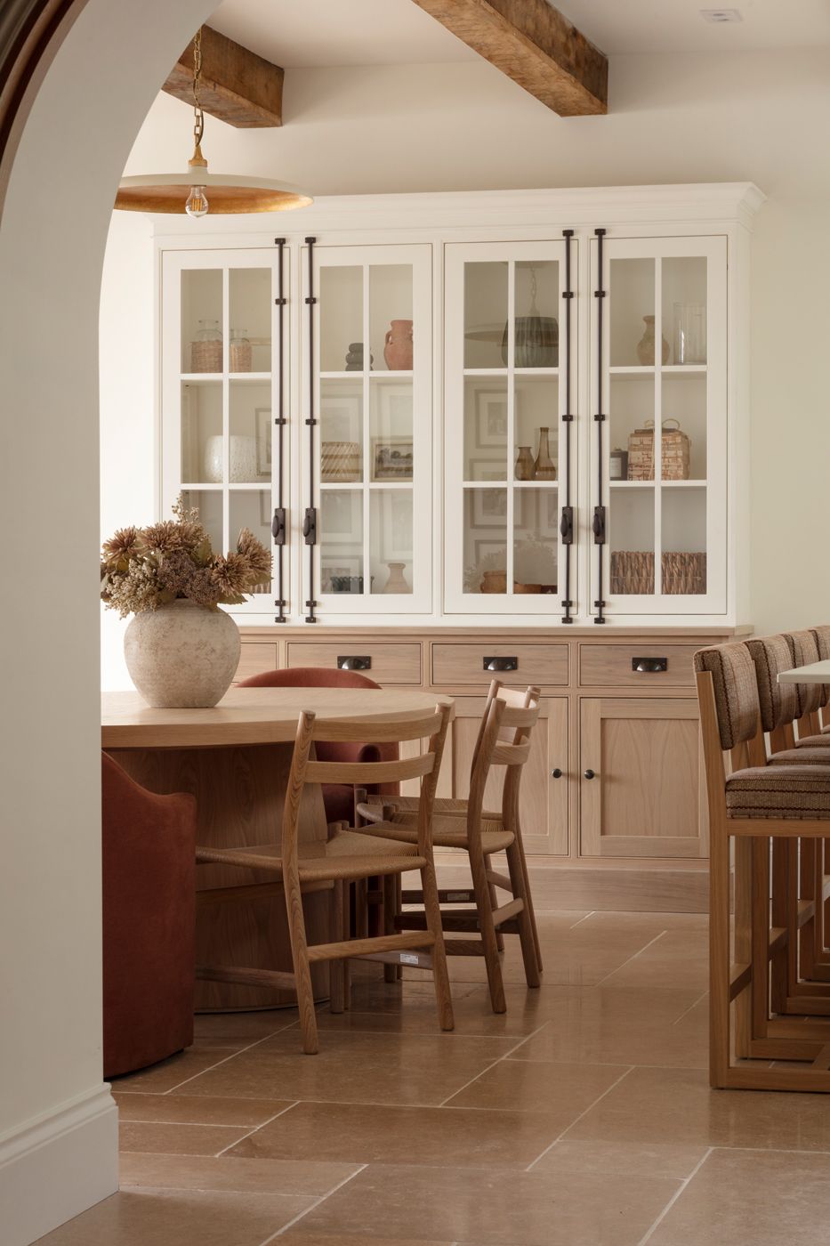 Modern farmhouse dining room features white cabinetry, wood beams, and natural stone flooring in a neutral color palette.