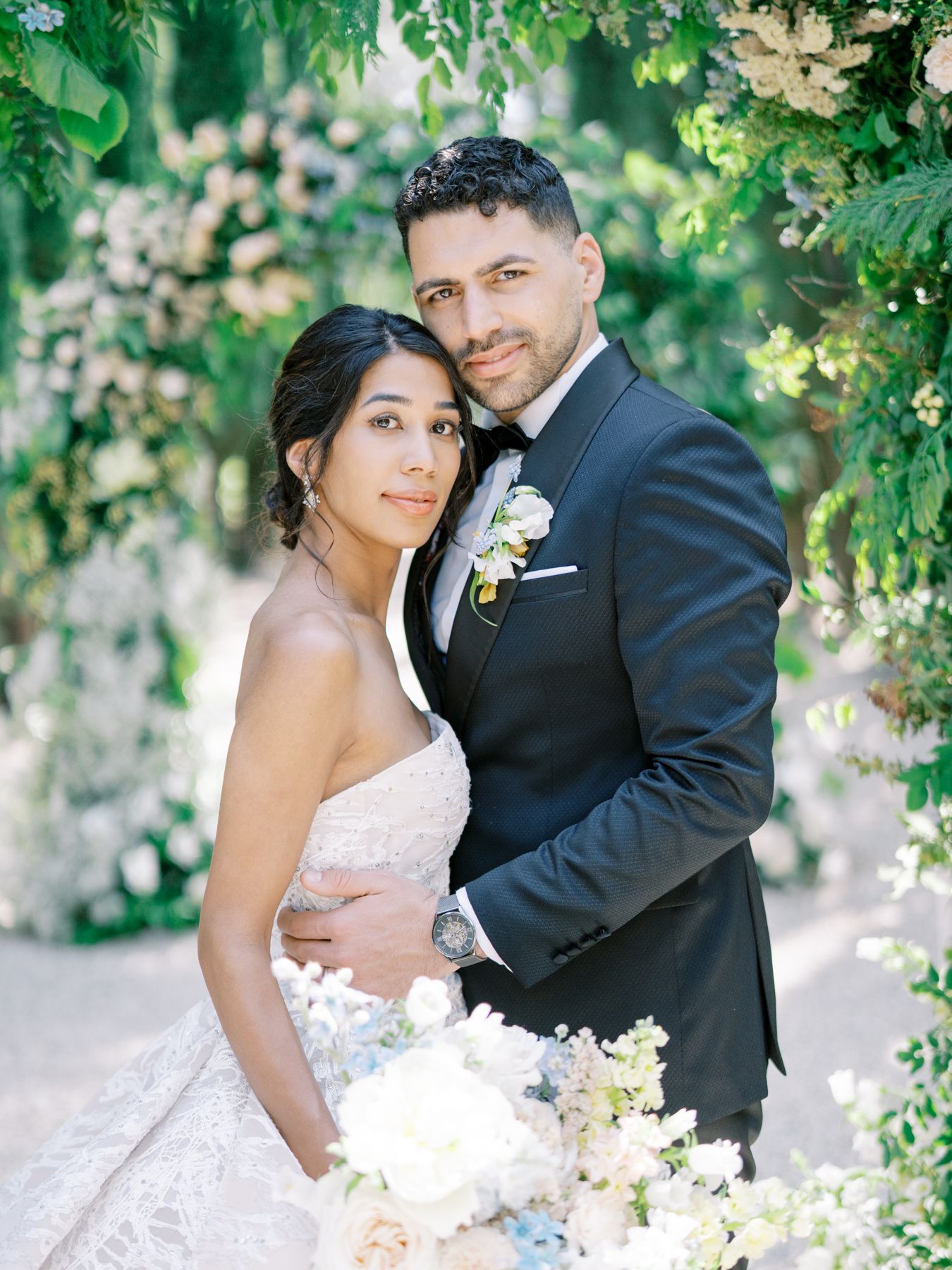 Romantic wedding portrait in a lush garden setting with white floral arrangements.