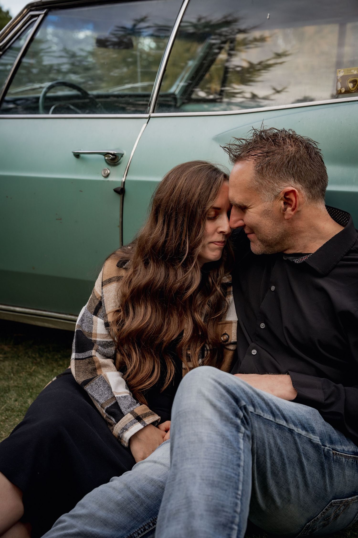 Intimate couple's portrait against vintage turquoise car showing tender moment.