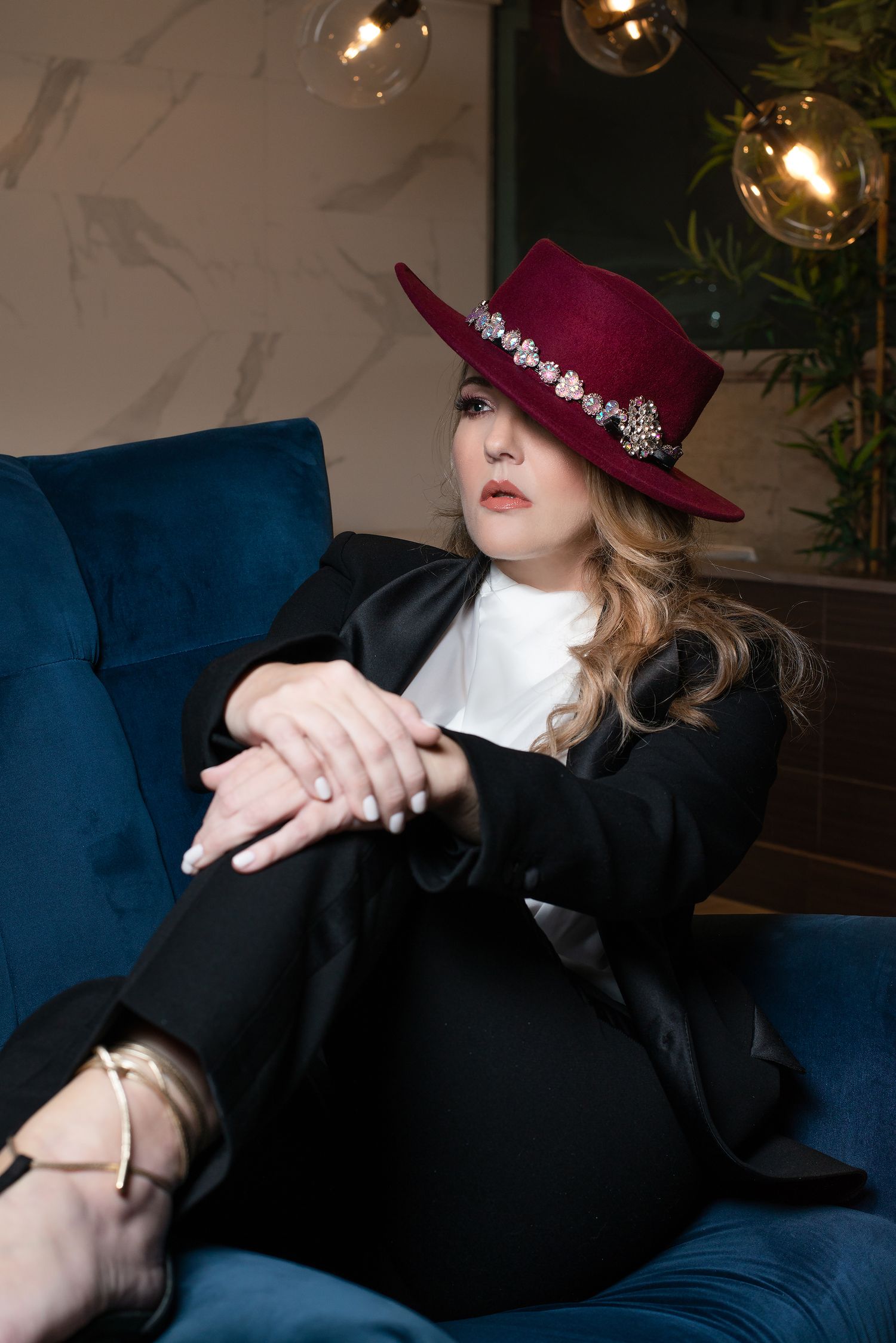 Fashion portrait with burgundy hat and black suit on blue velvet couch.