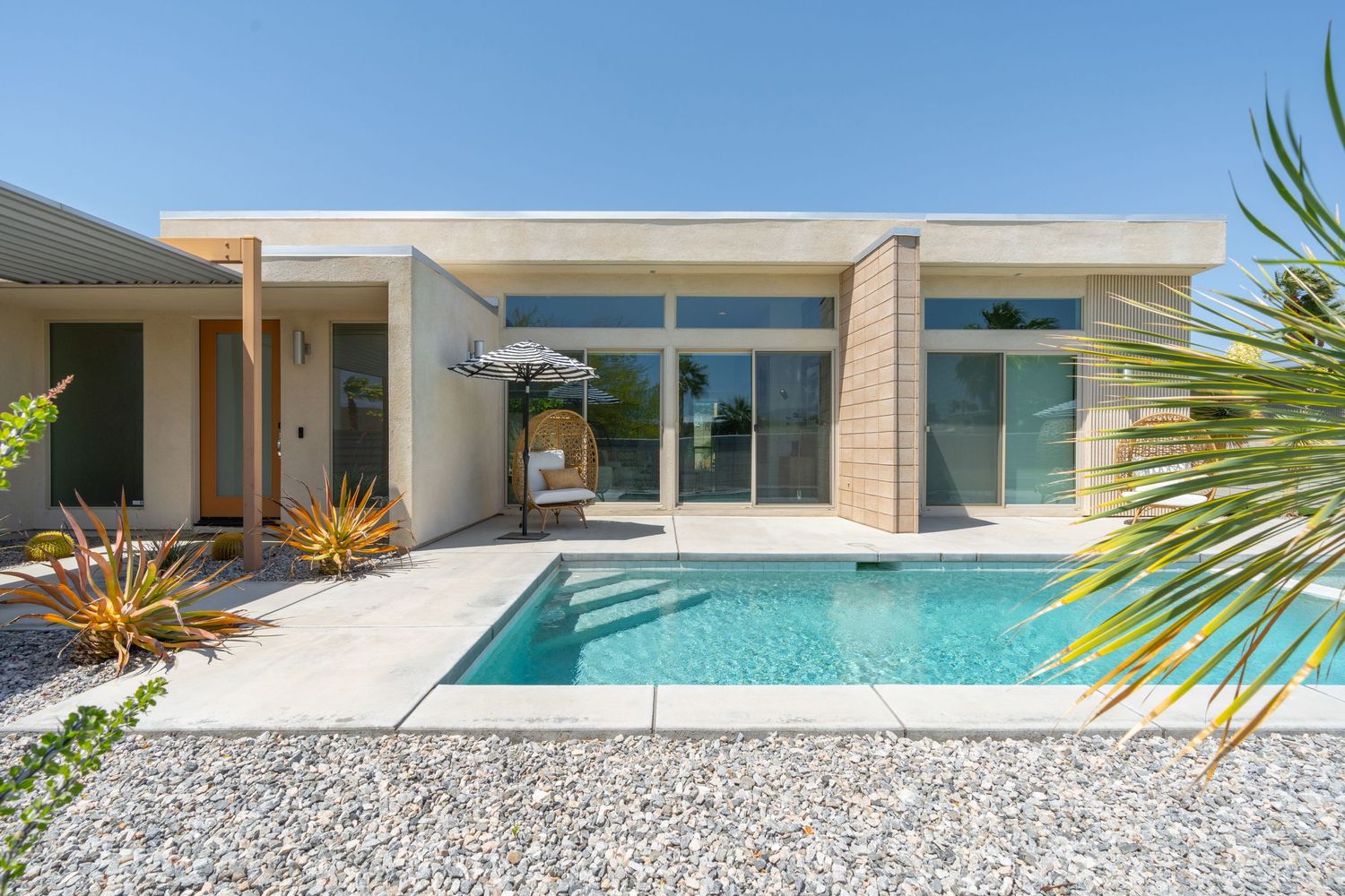 Modern minimalist house exterior with pool and glass walls surrounded by desert landscaping.