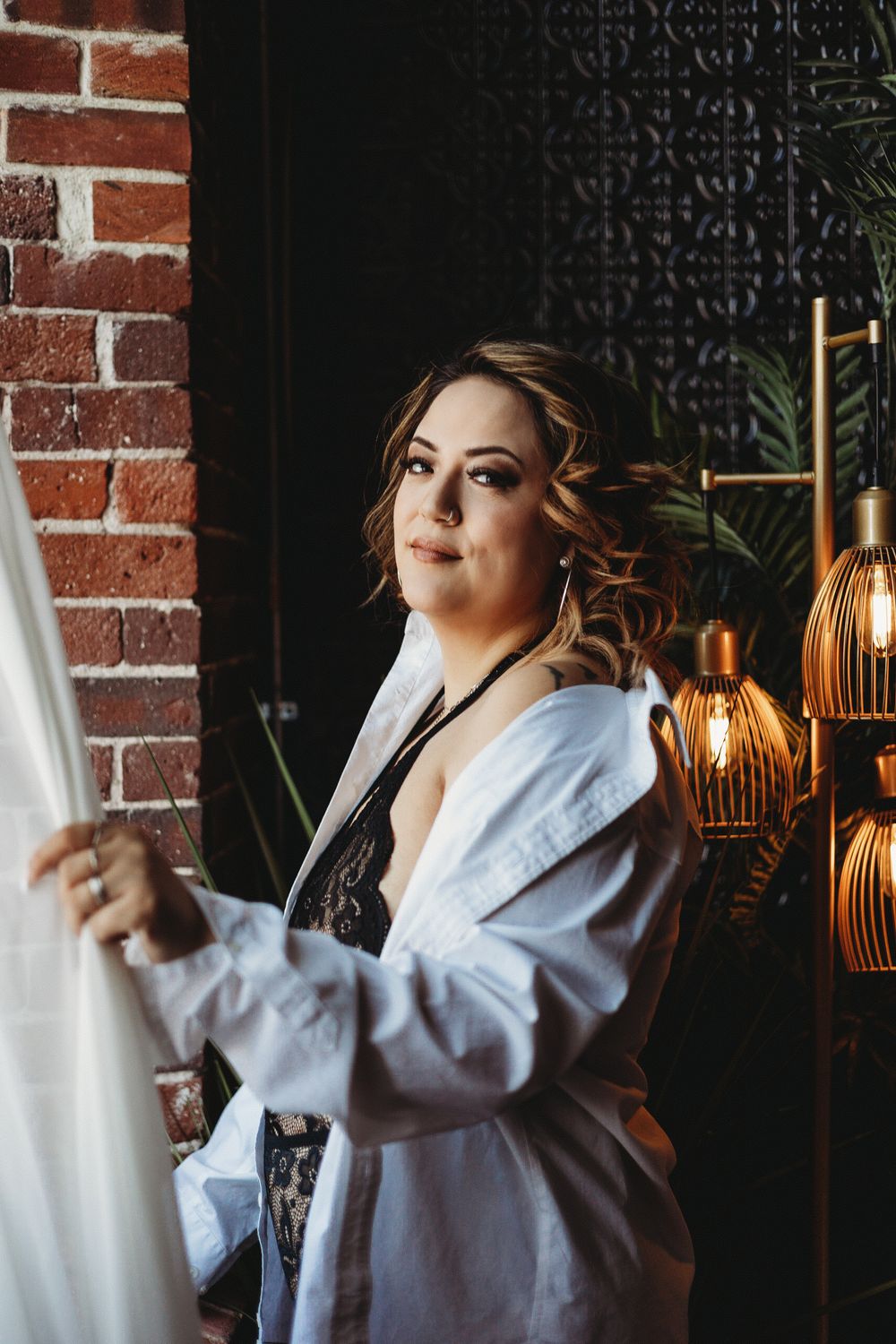 Person posing in white robe against brick wall with decorative lighting fixtures.