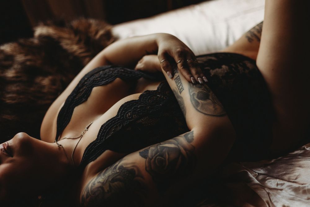 Artistic boudoir photo in black lingerie with soft lighting and shadows on white bedding.