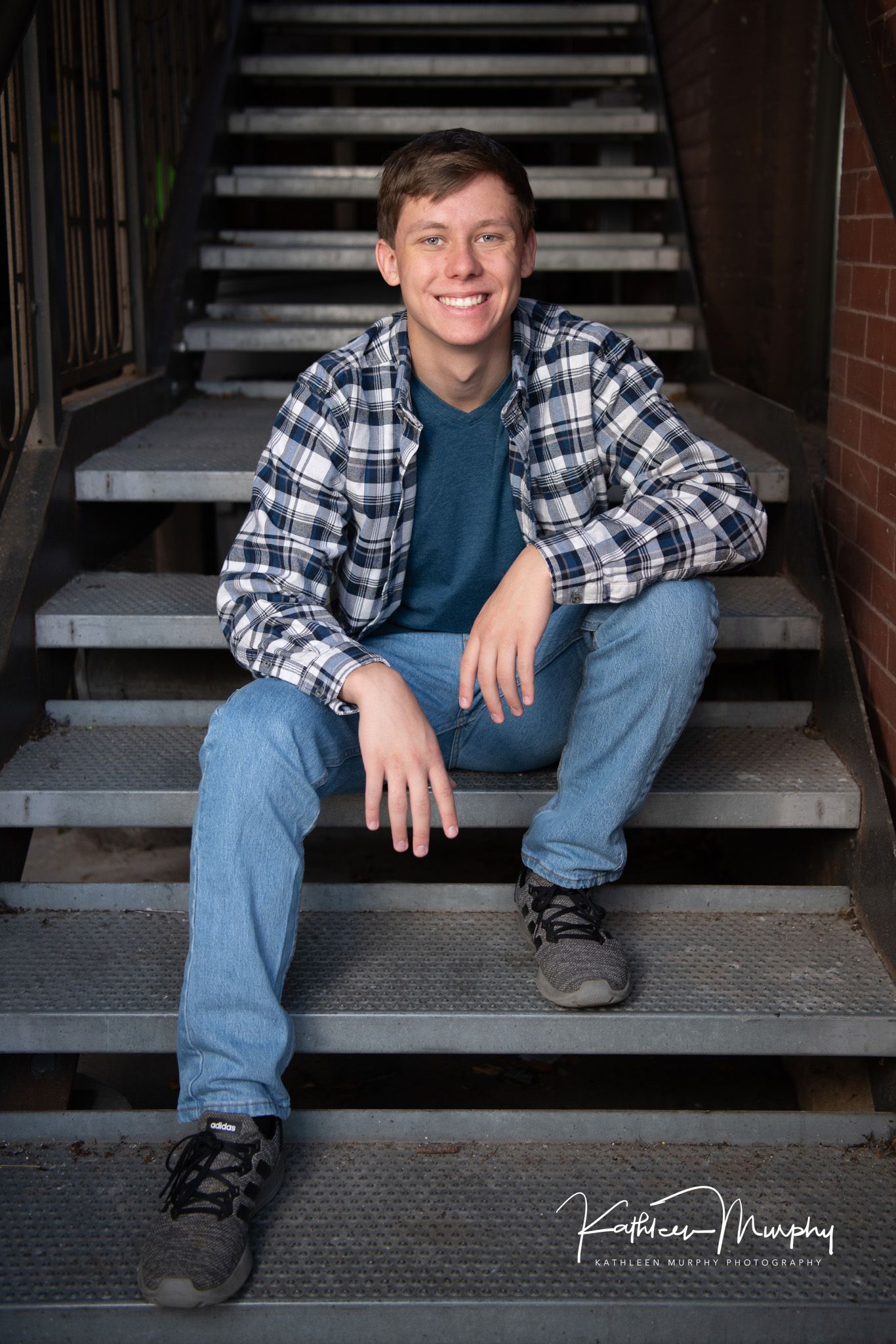 Person sitting on metal staircase wearing plaid flannel shirt and jeans in casual pose.