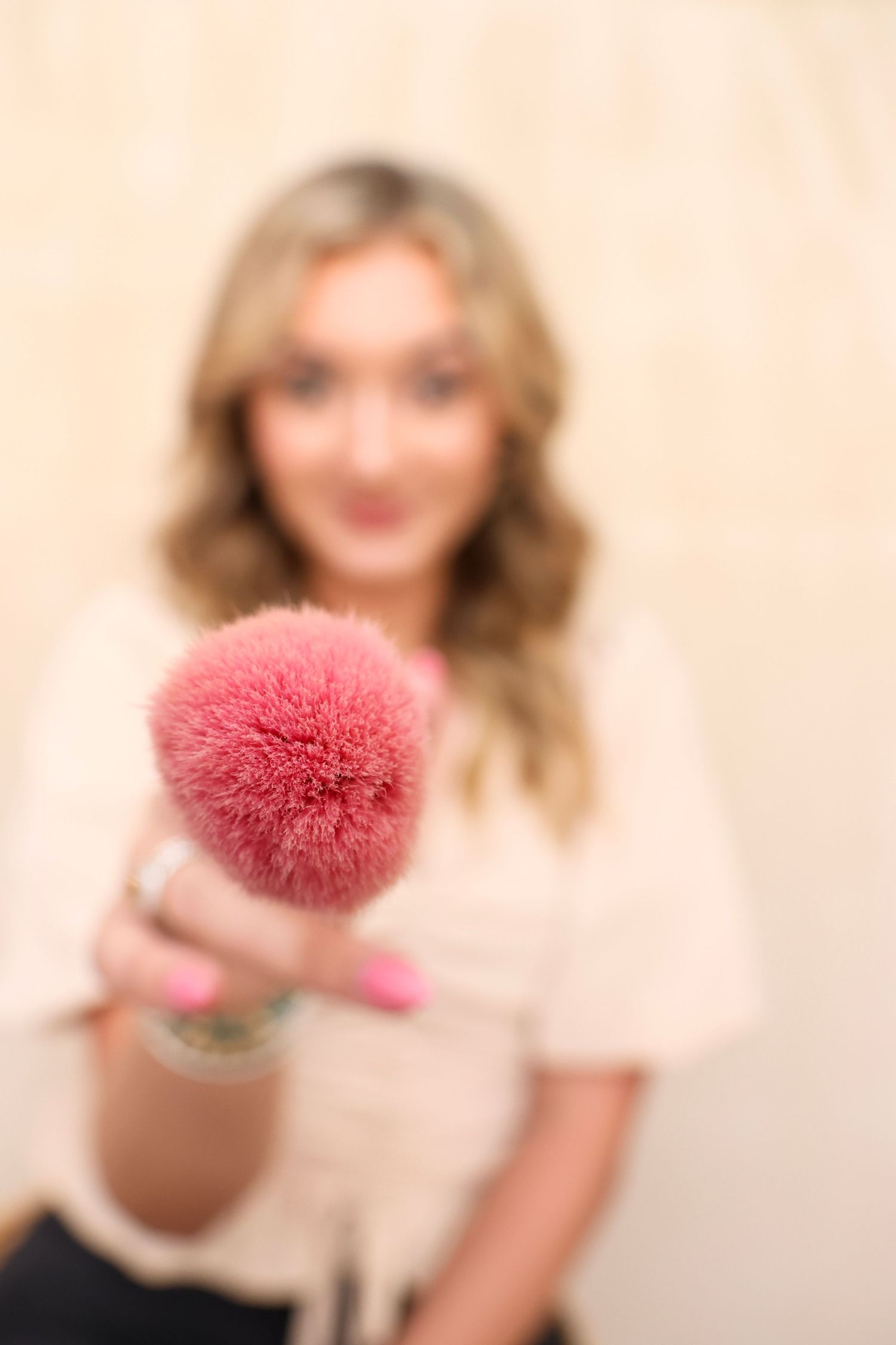 Pink makeup brush or powder puff against neutral background.