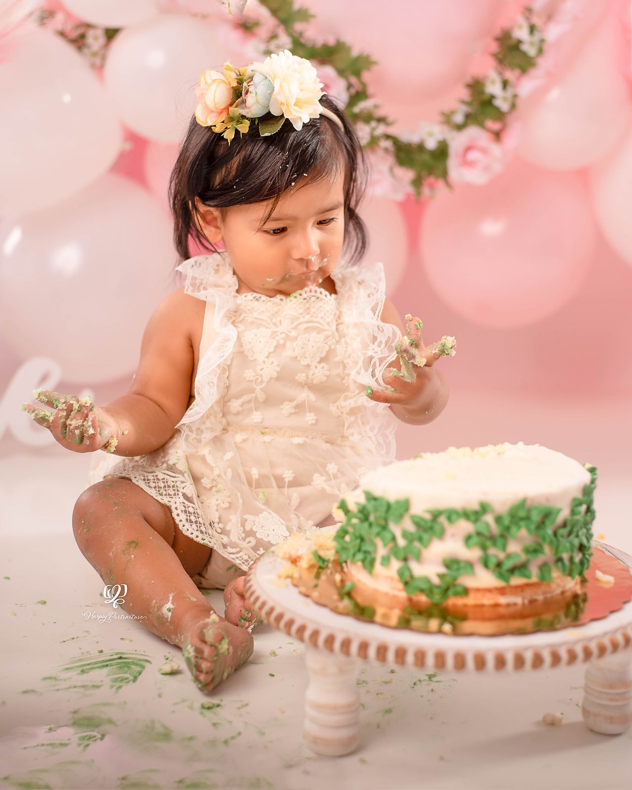 One year old baby girl eating cake for birthday photos, pink & white balloons with leaves; South Carolina photographer