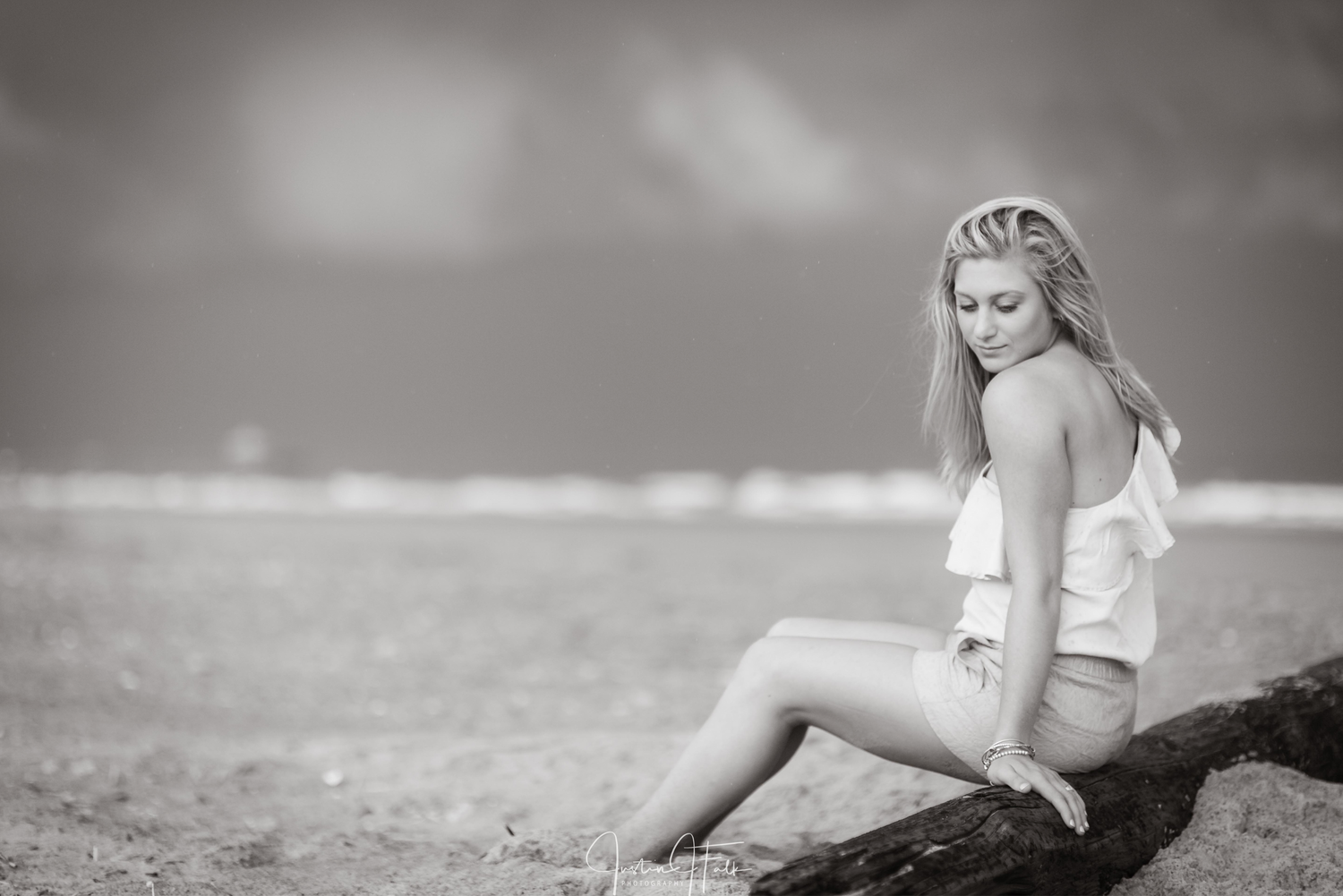 girl sits on drift wood with toes in the sand