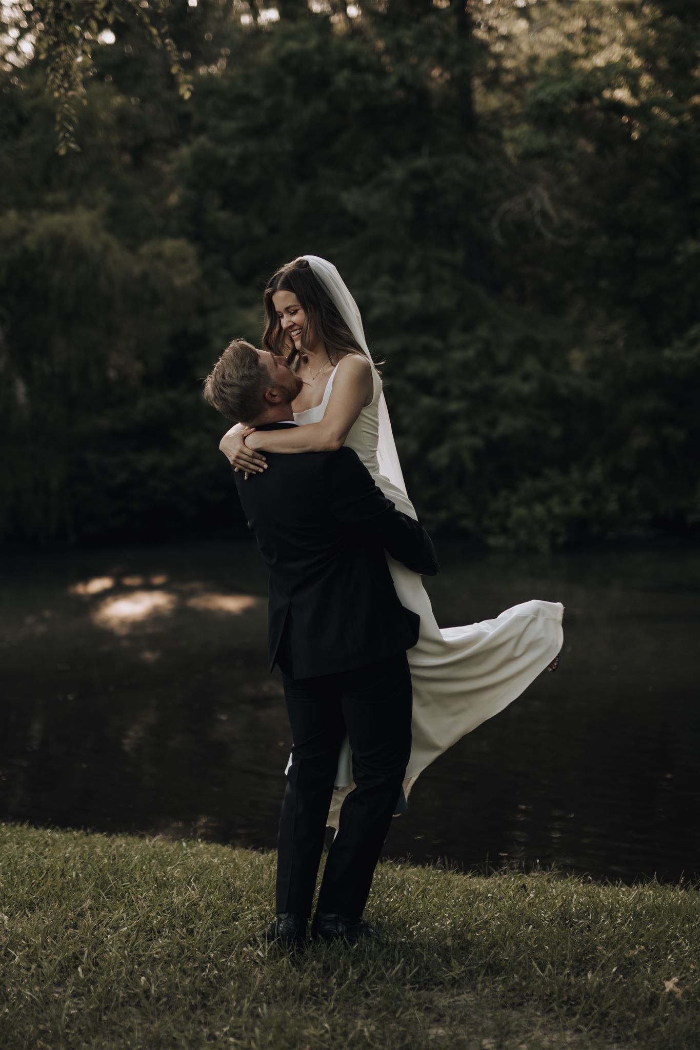 Romantic couple embrace in an intimate moment by a pond at sunset.