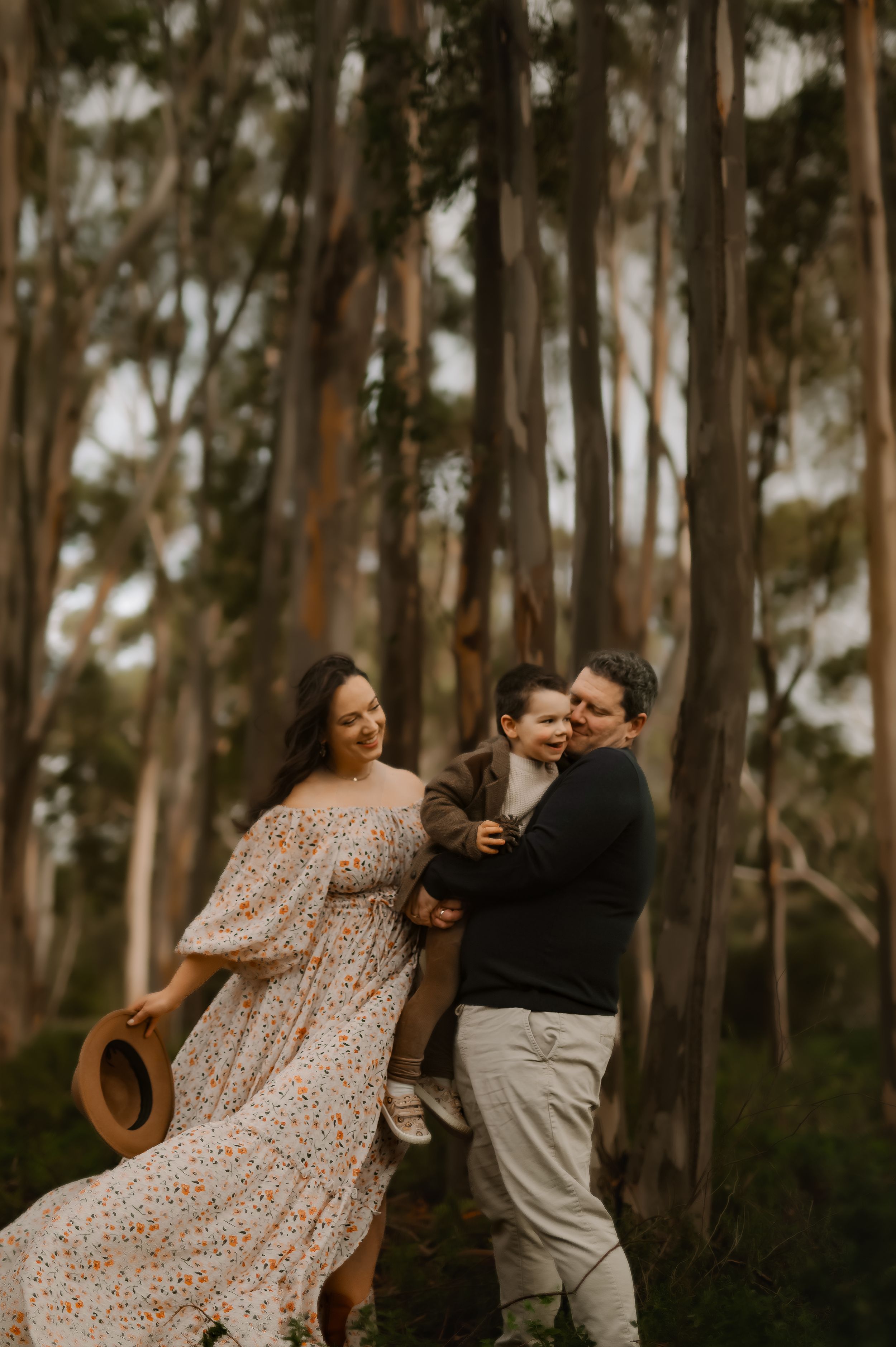 Family playing and dancing together joyfully among tall eucalyptus trees in a forest setting.