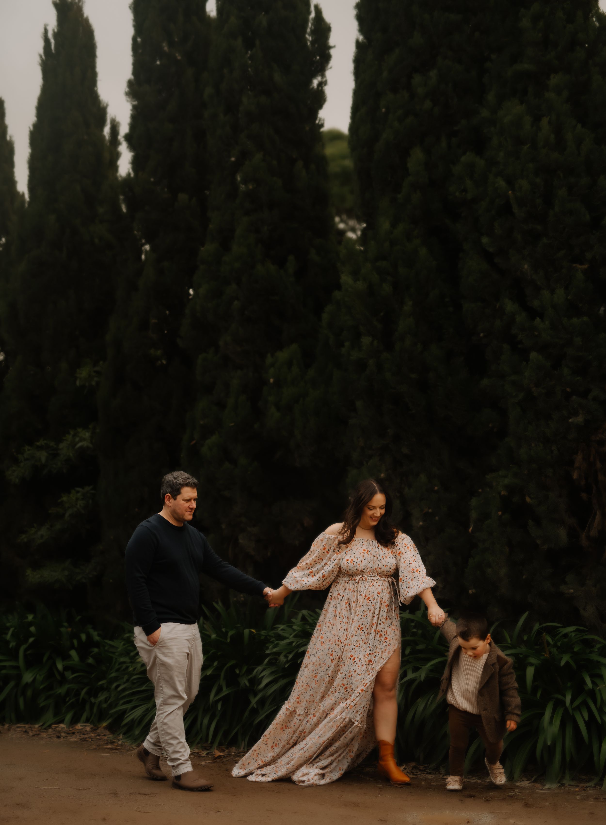 Family walking together through a garden path lined with tall cypress trees at dusk.
