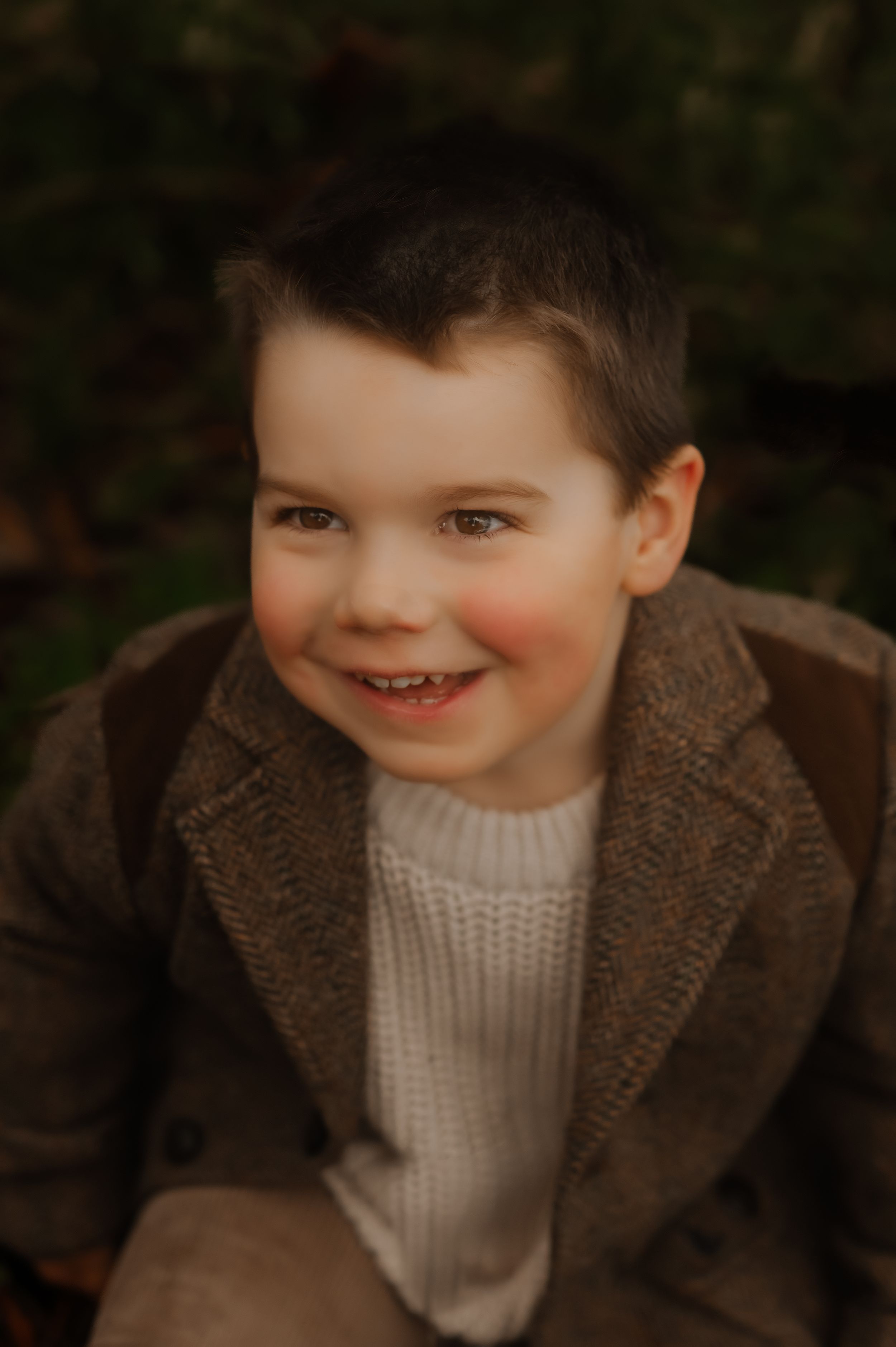 Close-up portrait of a smiling child wearing a brown coat and cream knit sweater.