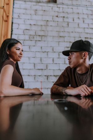 Couple in casual brown outfits share tender moments at a white brick wall setting.