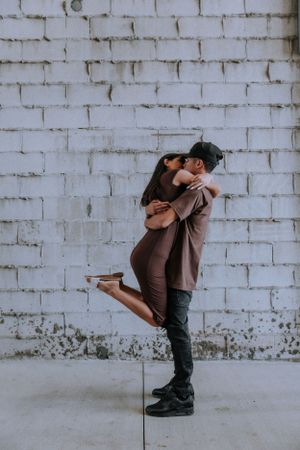 Playful couple photography sequence showing lifting poses against white brick wall.