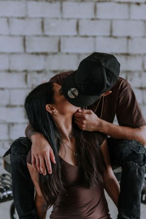 Romantic couple in brown attire share intimate moments against white brick wall.