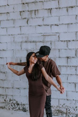 A couple performs a playful dance sequence against a white brick wall, showing fluid movement and coordination.