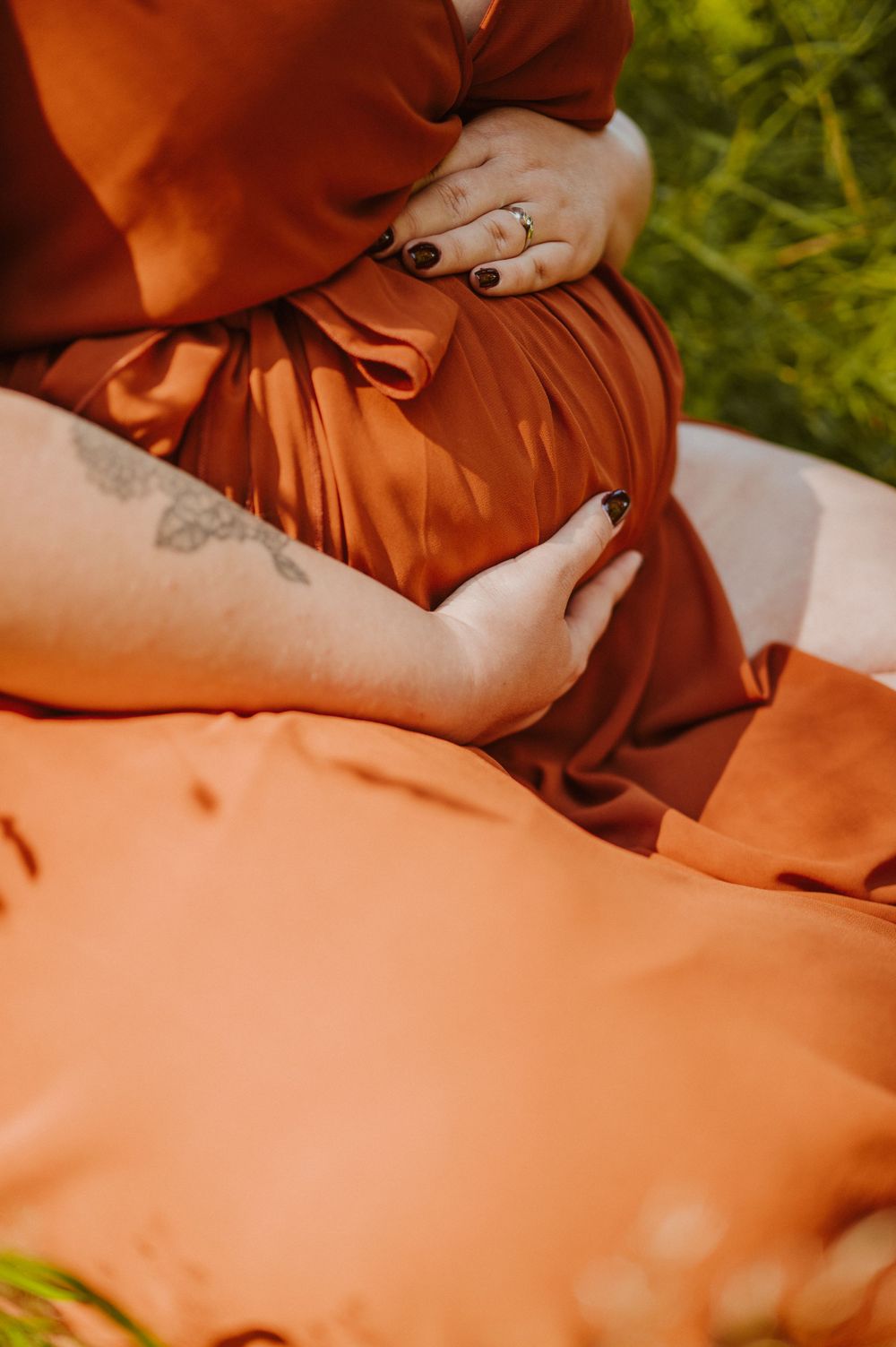 Close-up of hands gently resting on a rust-colored dress fabric showing delicate details and texture.