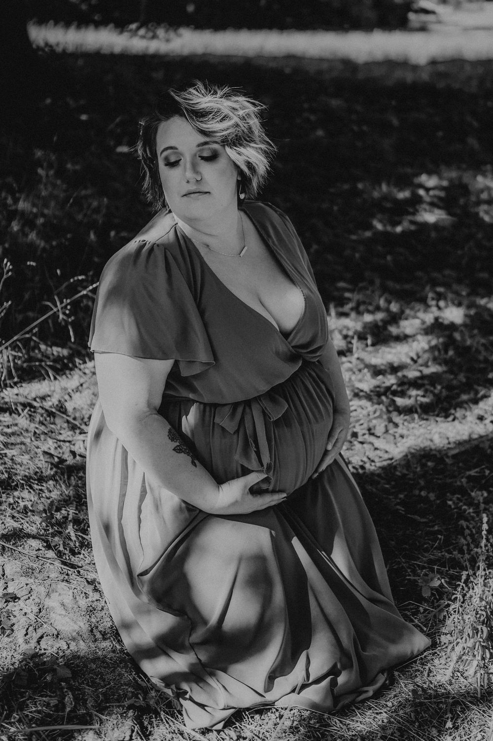 Black and white portrait in dappled sunlight showing a flowing dress and natural setting.